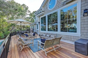 A wooden deck with outdoor furniture, large windows, and a view of trees.
