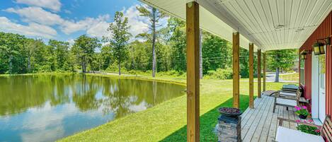 A covered deck with wooden pillars, a pond, and a lawn.
