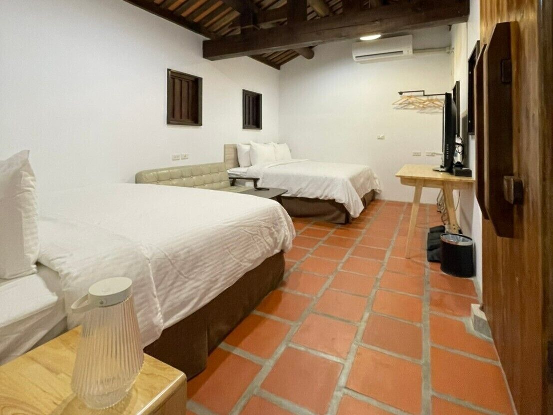 Una habitación con dos camas, una mesa de madera, una lámpara y un televisor.