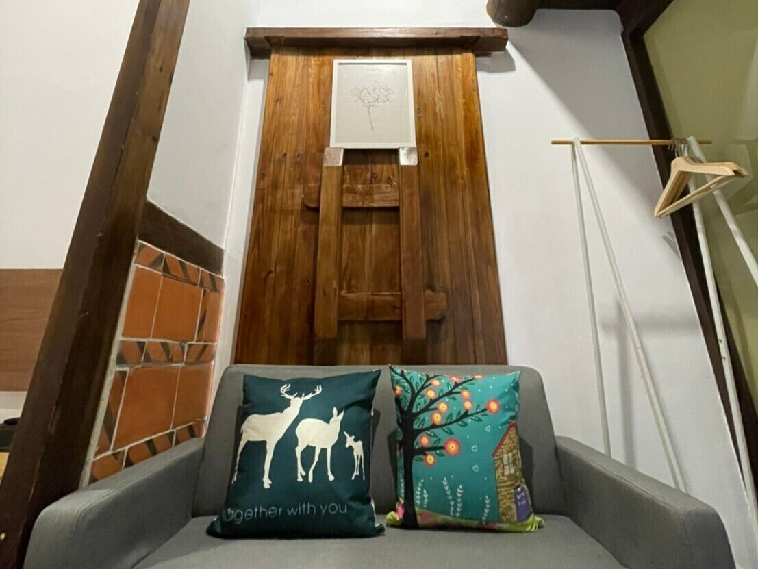 Una escalera con dos almohadones decorativos en un sofá, una puerta de madera con una obra de arte pequeña y un perchero de madera.