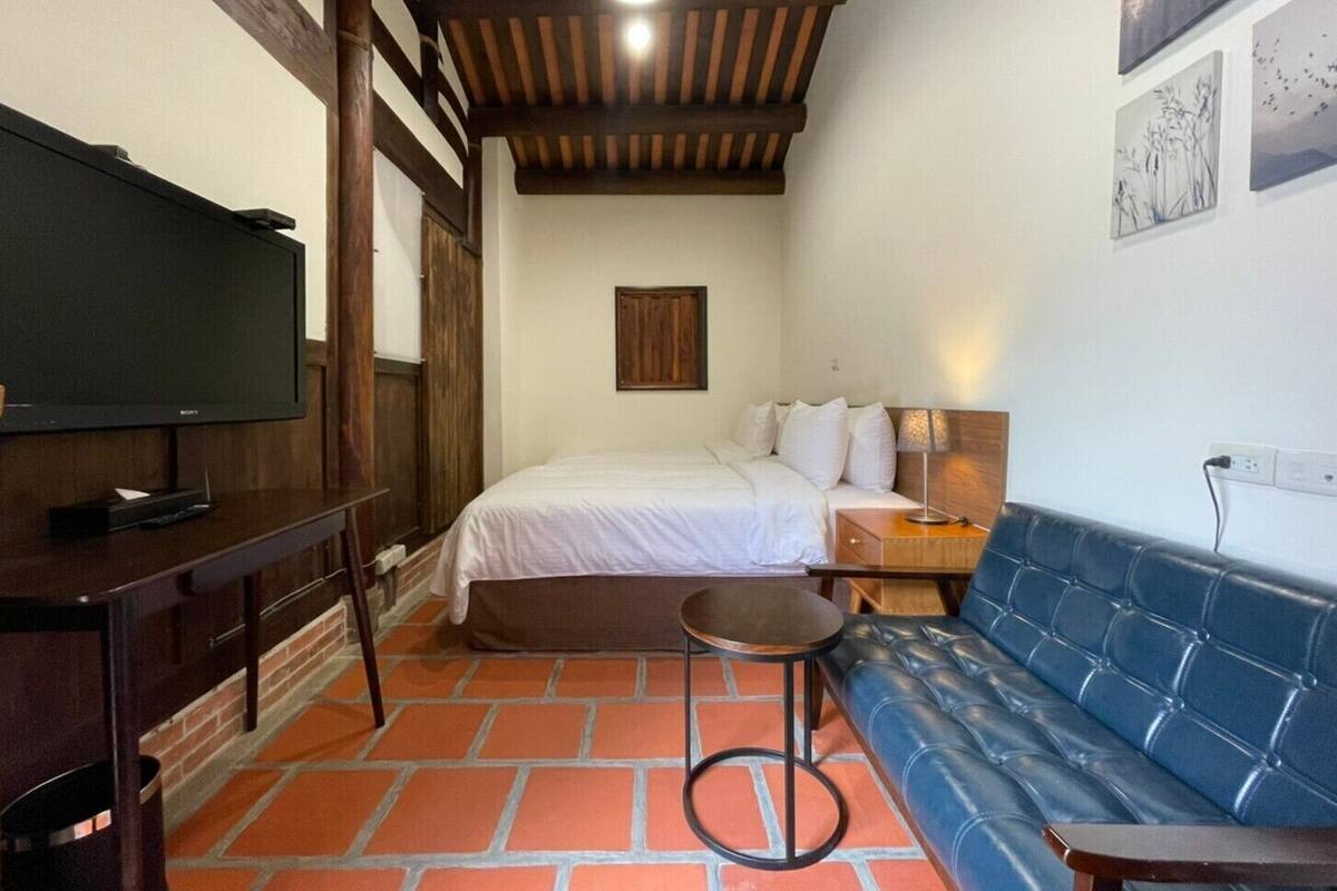 A hotel room with a bed, a TV, a blue sofa, and a small table.