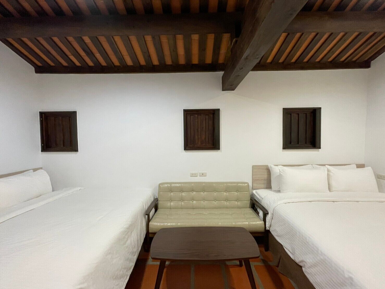 Habitación de hotel con dos camas, un sofá y techo de madera.