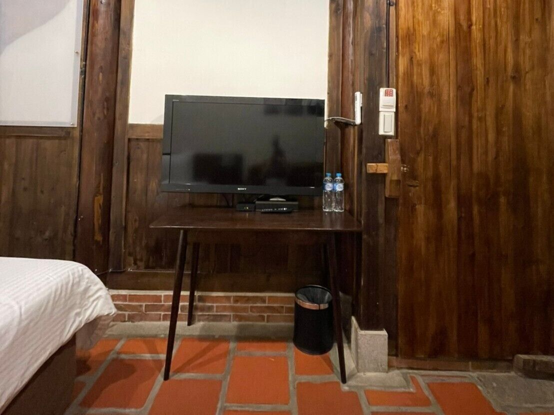 Una habitación con una cama, un escritorio de madera y un cubo de basura.