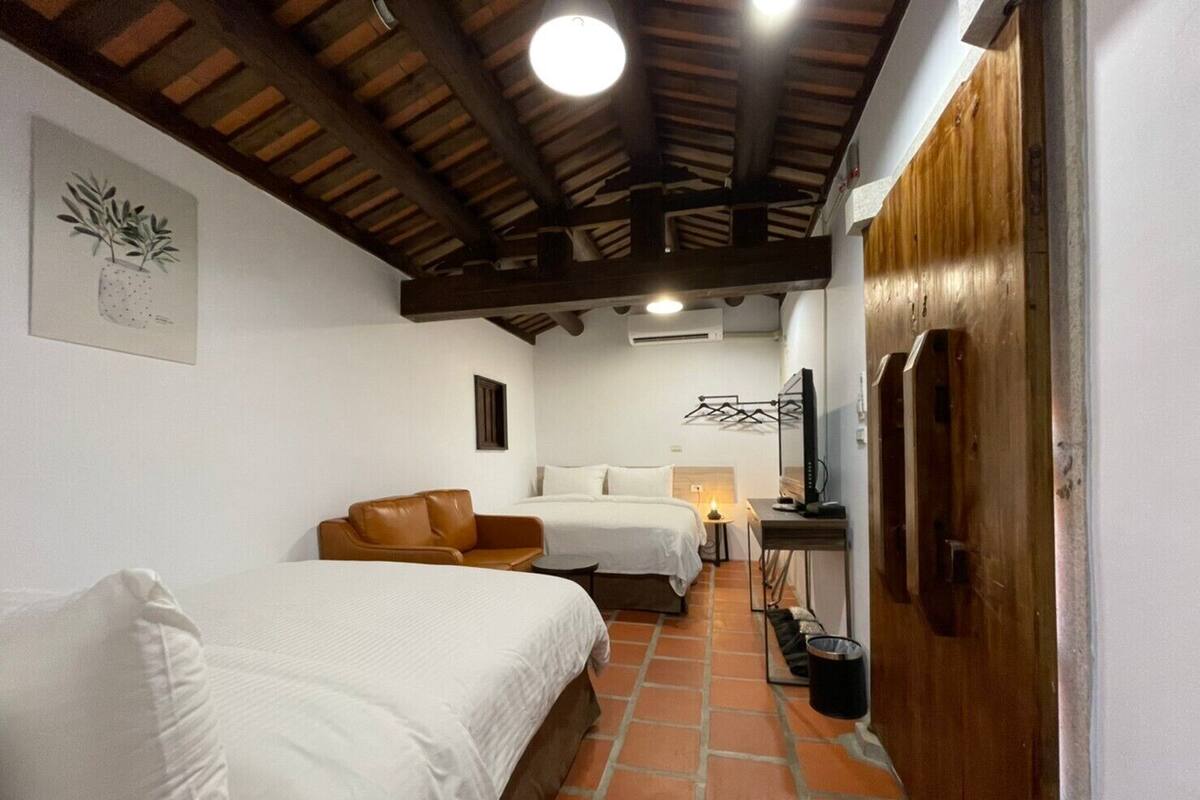 A hotel room with two beds, a brown leather sofa, a TV, and a wooden door.