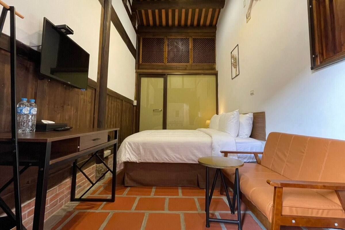A small, cozy room with a bed, a wooden desk, a small table, and a sofa.