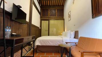 A small, cozy room with a bed, a wooden desk, a small table, and a sofa.