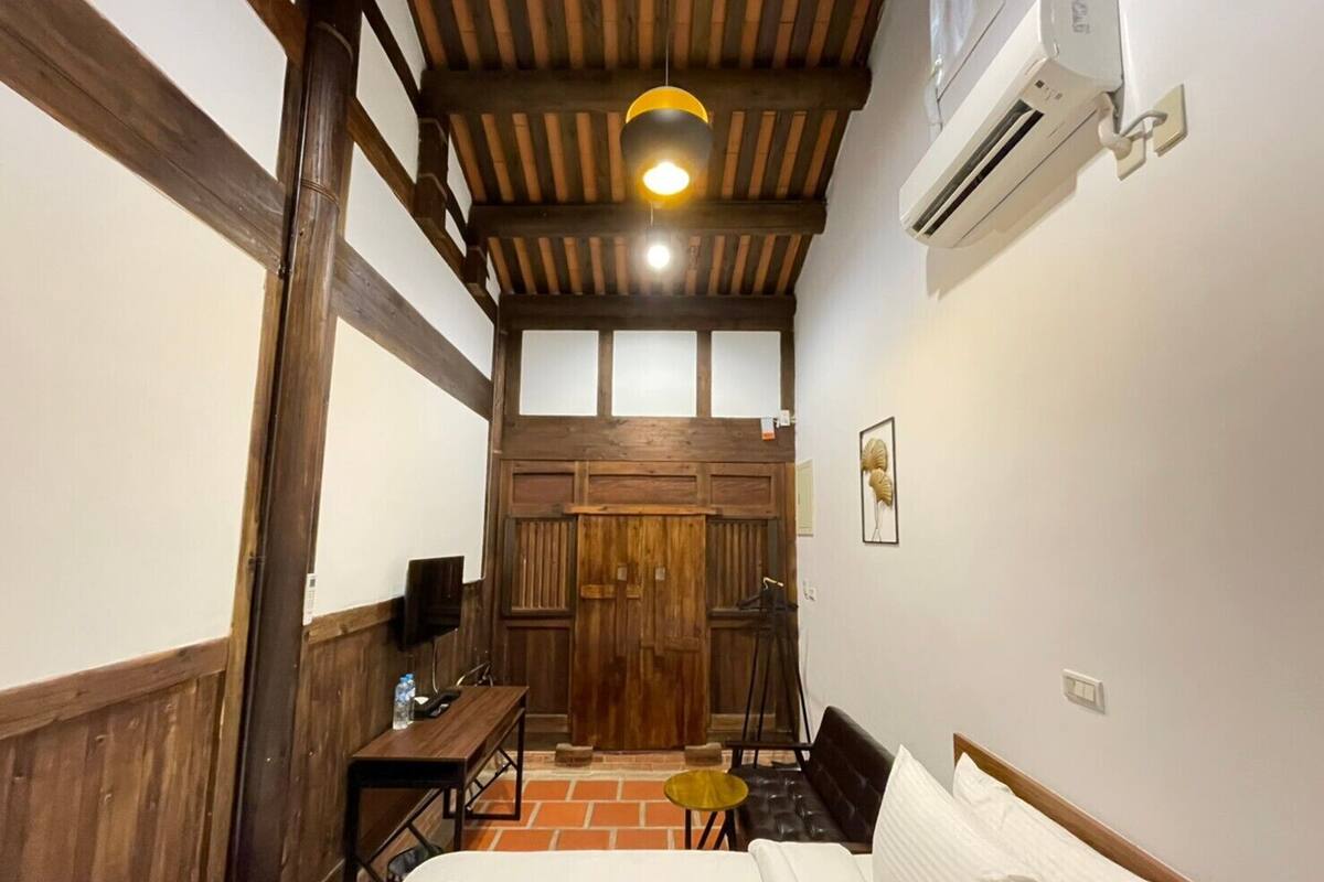 A room with a bed, a desk, a chair, a small table, and a hanging light fixture.