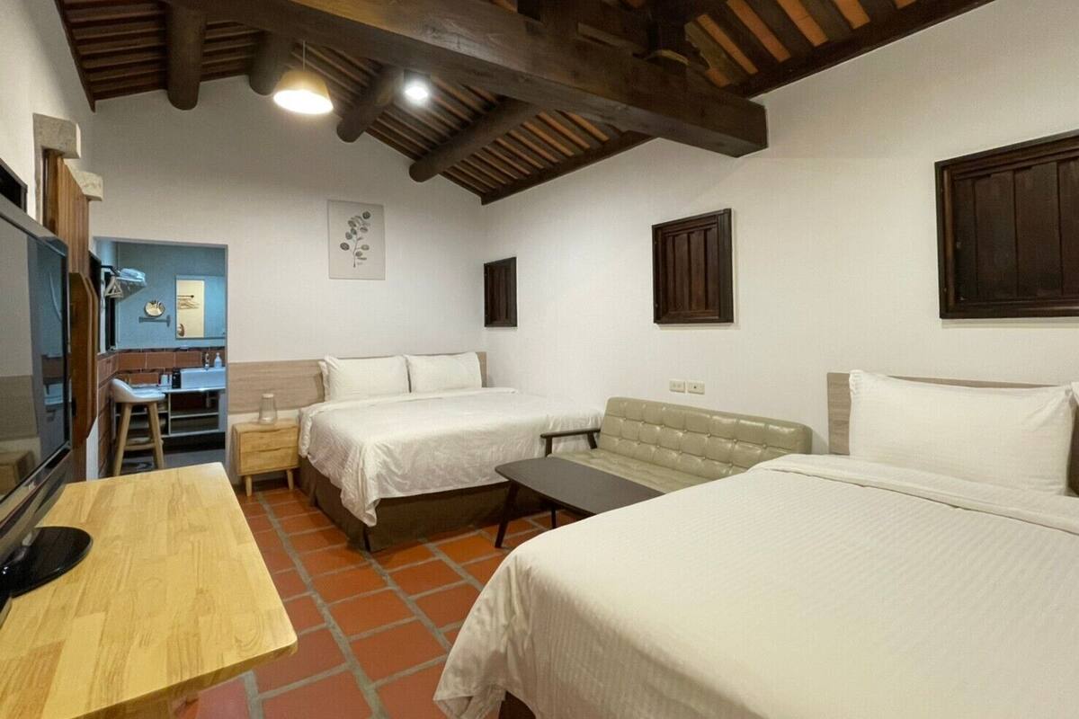 A room with two beds, a wooden table, a small stool, a desk, and a mirror.