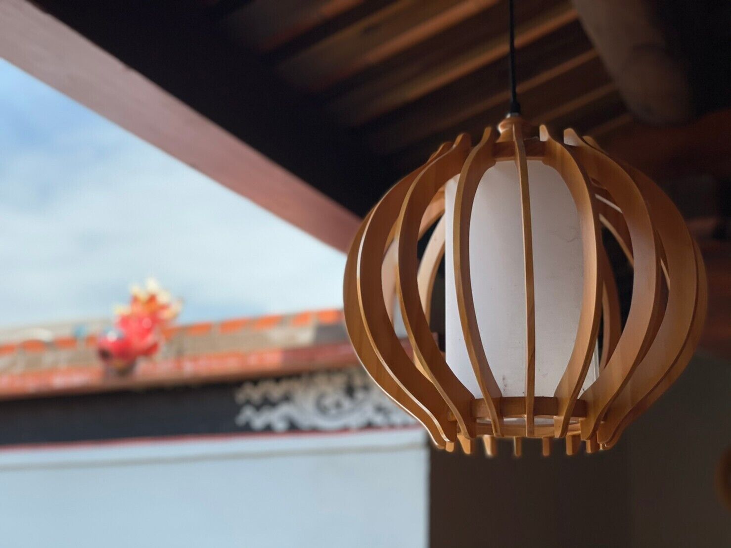 Um lanterna de madeira pendurada, com interior branco, suspensa por uma estrutura de vigas de madeira.