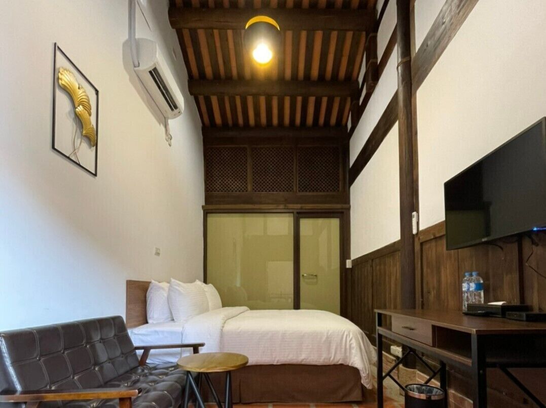 A bedroom with a bed, a sofa, a small table, a TV, and a window.