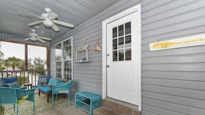 A covered porch with blue wicker furniture, a white door, and a ceiling fan. - Tybee Paradise Beach House for Families, Pet Friendly (Tybee Island)