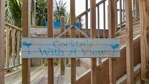 A wooden sign with the text "Cocktails With A View" hanging on a wooden railing. - Tybee Paradise Beach House for Families, Pet Friendly (Tybee Island)