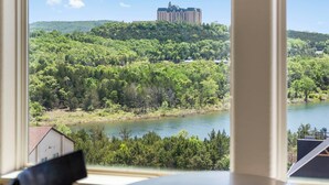 A view of a hotel with a large building on a hill, surrounded by lush greenery and a body of water. - Branson Getaway • Sunroom + Balcony + Stunning Table Rock Lake View (Branson)