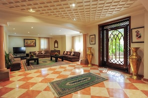 A spacious living room with a checkered floor, a sofa set, a television, and a large decorative vase. - Amina Resort & Spa (Marrakech)