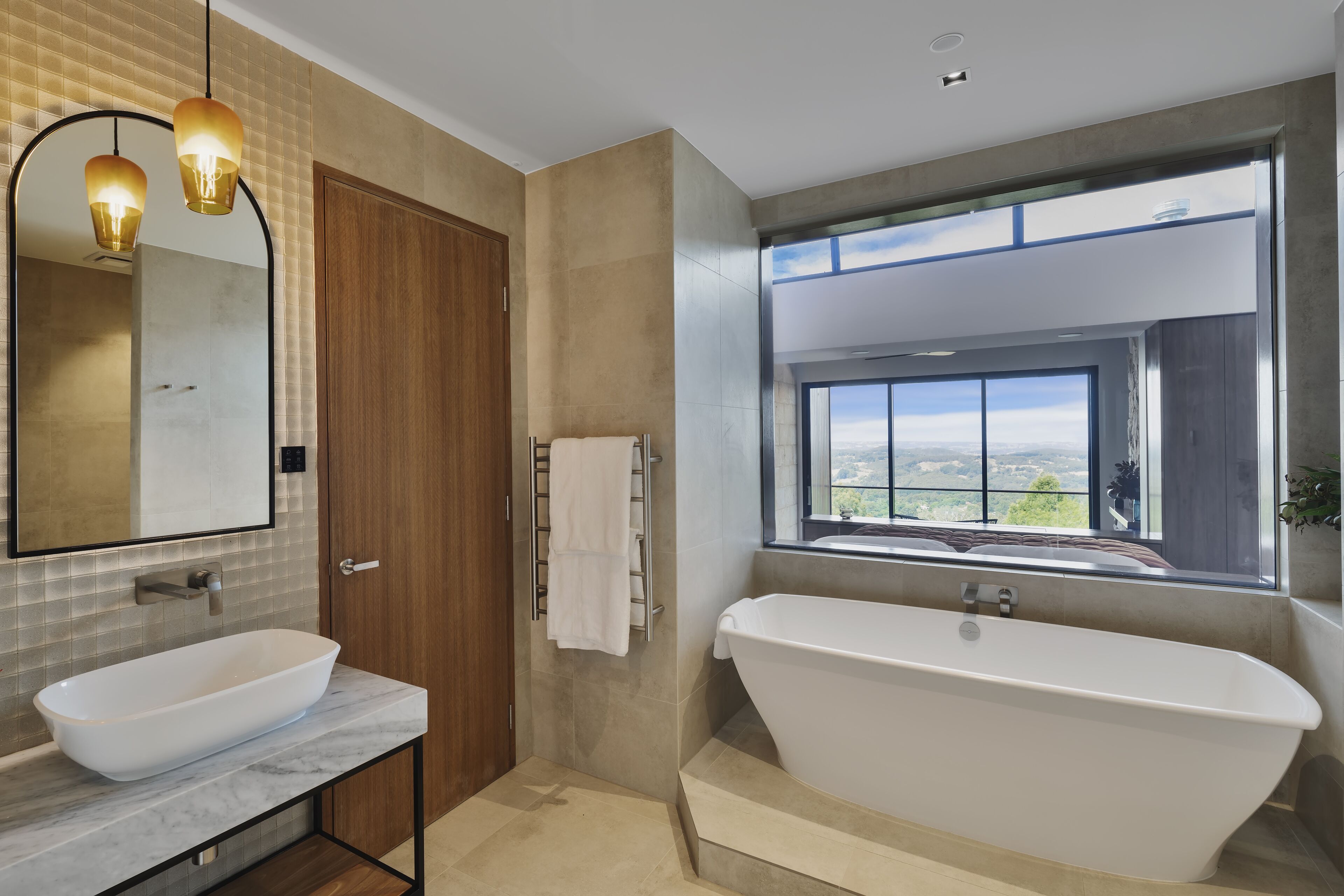 A modern bathroom with a freestanding bathtub, a large mirror, and a window offering a scenic view.