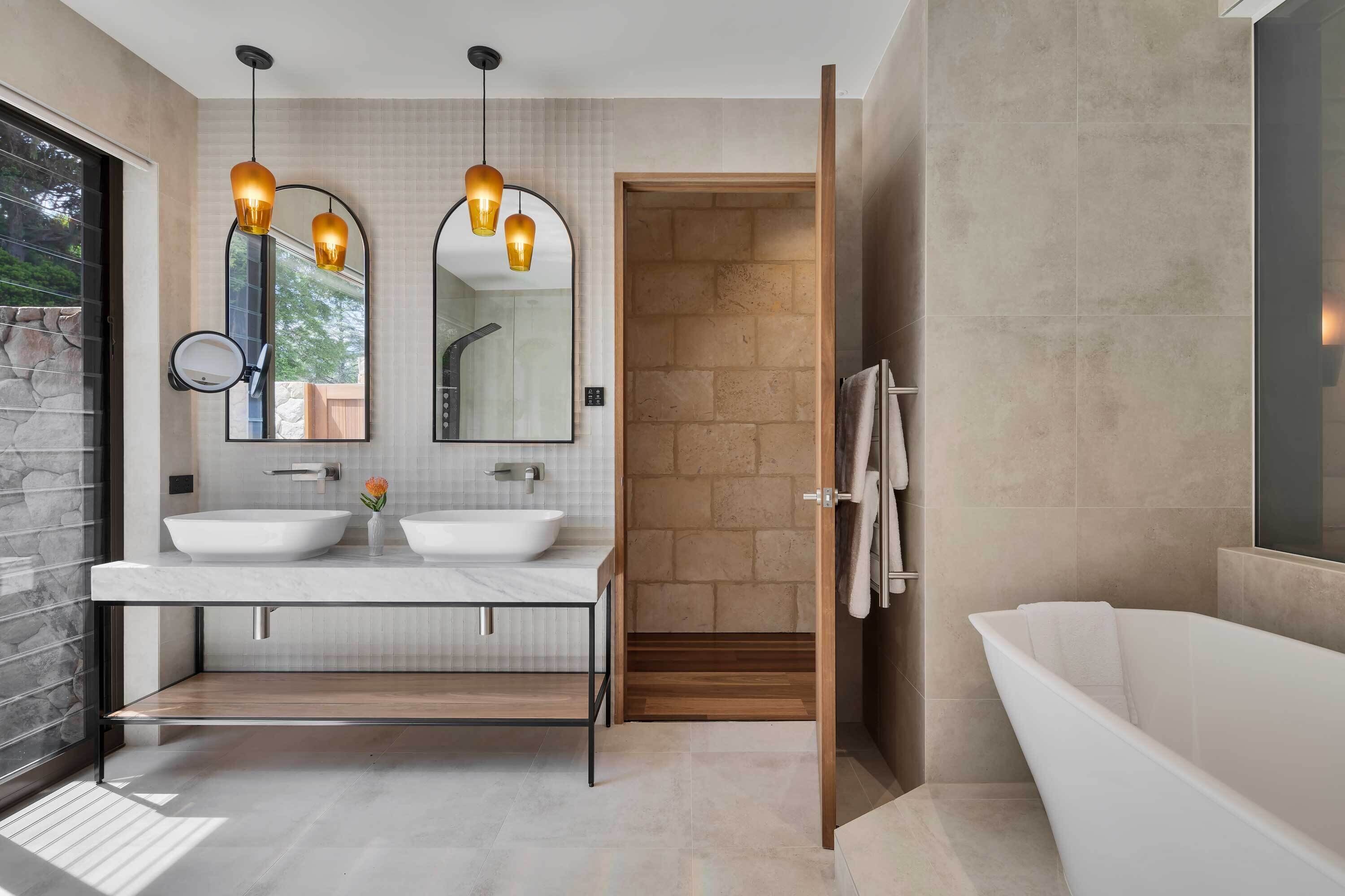 A modern bathroom with two sinks, a large mirror, and a freestanding bathtub.
