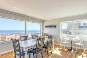 Uma área de refeições com vista para o oceano, piso de madeira e uma mesa com cadeiras.