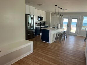 Cozinha moderna com ilha central, eletrodomésticos de aço inoxidável e vista para o oceano através de grandes janelas.