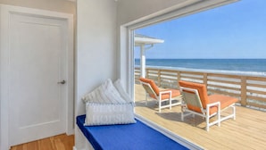 Un balcon avec vue sur l’océan, une porte et deux fauteuils de relaxation avec des coussins.