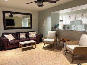 A living room with a brown leather sofa, two armchairs, a wooden coffee table, and a large mirror.