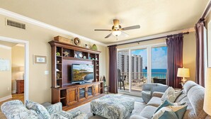Uma sala de estar espaçosa com uma televisão grande, assentos confortáveis e uma varanda com vista para a cidade.
