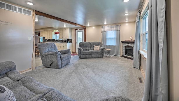A living room with grey sofas, a fireplace, and a kitchen in the background. - 'Rise and Shine Farm' in Goshen w/ BBQ & Fire Pit! (Goshen)