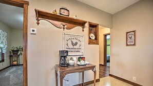A hallway with a wooden table holding a coffee maker, cups, and a sign. A clock and a framed picture are on the wall. - 'Rise and Shine Farm' in Goshen w/ BBQ & Fire Pit! (Goshen)