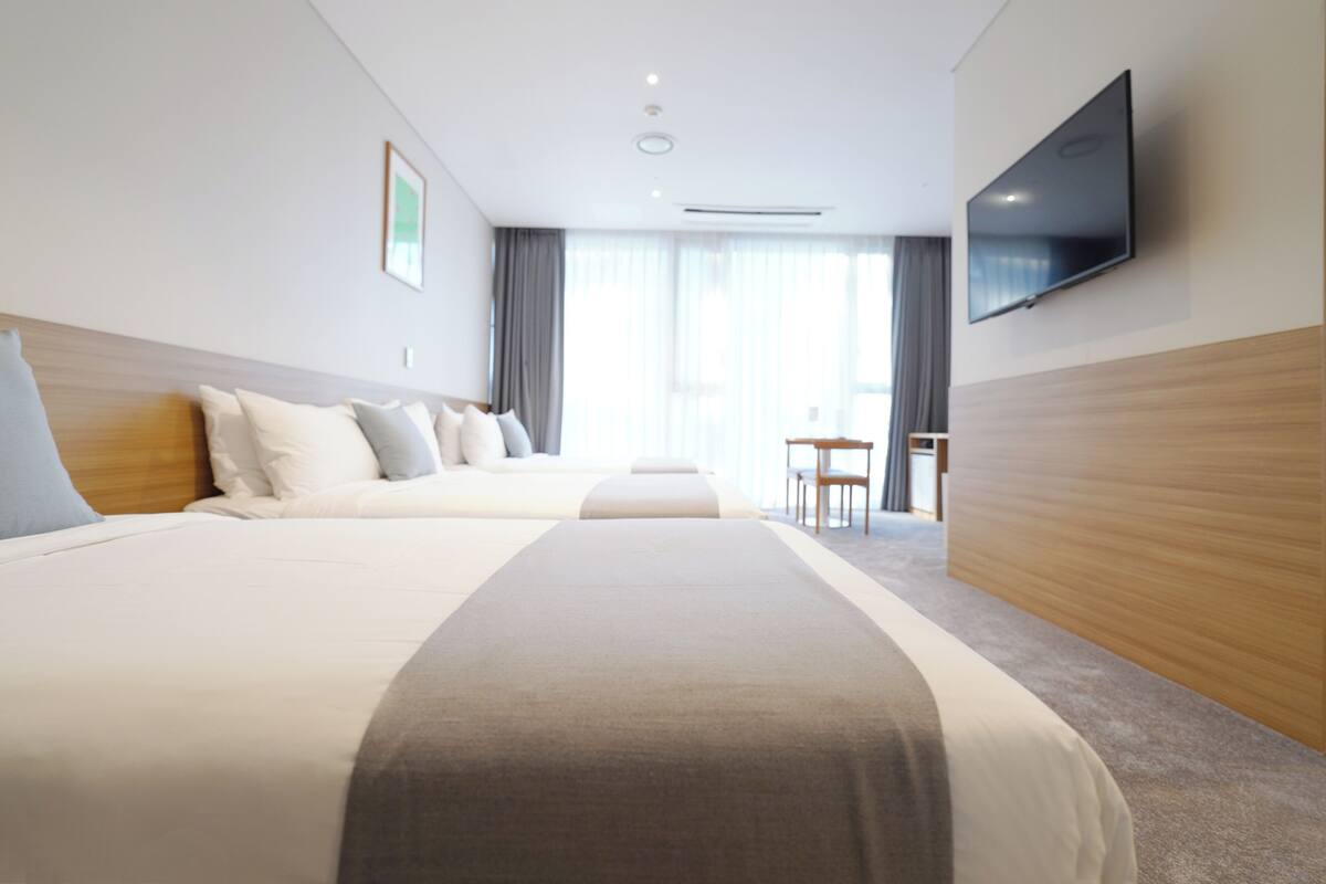 A hotel room with two beds, a TV mounted on the wall, a desk, and a chair.