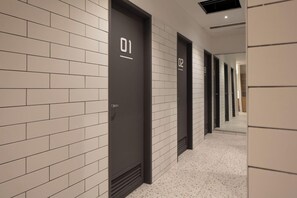 Un pasillo con puertas numeradas, paredes de azulejos blancos y suelo moteado.