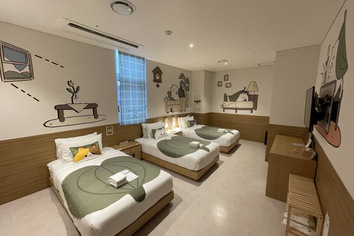 A hotel room with three beds, a small desk, and a television.