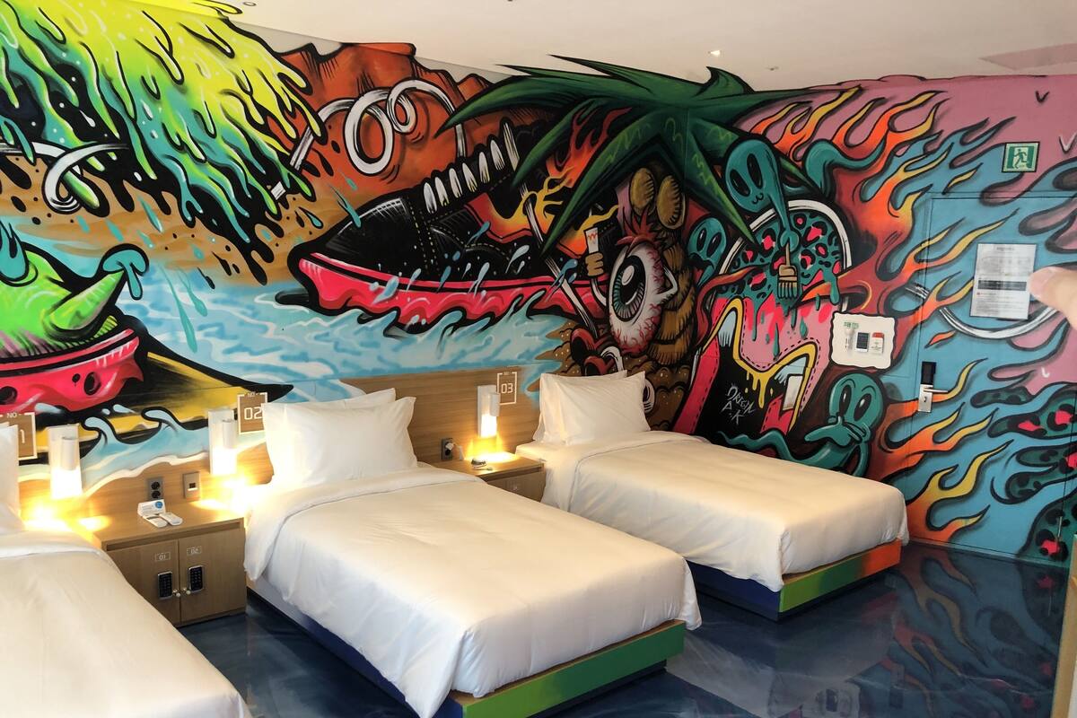 A hotel room with two beds, a mural on the wall, and a nightstand with a lamp.