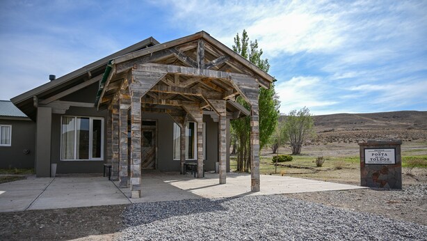 A rustic building with a wooden structure and a stone base, surrounded by gravel and sparse vegetation.