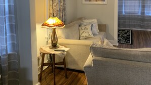 A cozy living room with a sofa, a small table with a lamp, a framed picture on the wall, and a window with curtains. - BEST⭐️6 SLEEPS+|3 BDR ENTIRE HOME💖FREE PARKING#Pet Friendly|Near Beaches CASINO (Atlantic City)