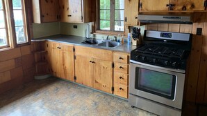 A kitchen with wooden cabinets, a stainless steel stove, and a window. - Cozy Camp on Lake Winni (Meredith)
