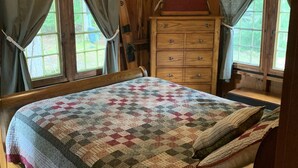 A wooden cabin bedroom with a bed, a dresser, and two windows with curtains. - Cozy Camp on Lake Winni (Meredith)