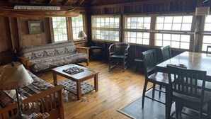 A rustic cabin interior with a sofa, chairs, a dining table, and a sign reading "Lake Winnipeg's Lake". - Cozy Camp on Lake Winni (Meredith)