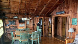 A wooden cabin interior with a dining table and chairs, a sofa, and a sign that reads "It's summertime". - Cozy Camp on Lake Winni (Meredith)