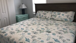 Ein Schlafzimmer mit Bett, Nachttisch, Lampe und Fenster.