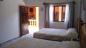 Une chambre avec deux lits, une armoire en bois, une fenêtre avec des rideaux et une porte donnant sur un espace extérieur.