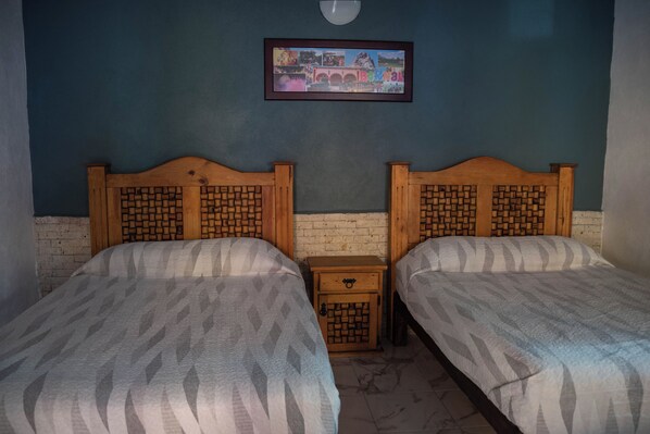 A room with two beds with wooden headboards, a small wooden nightstand between them, and a framed picture on the wall.