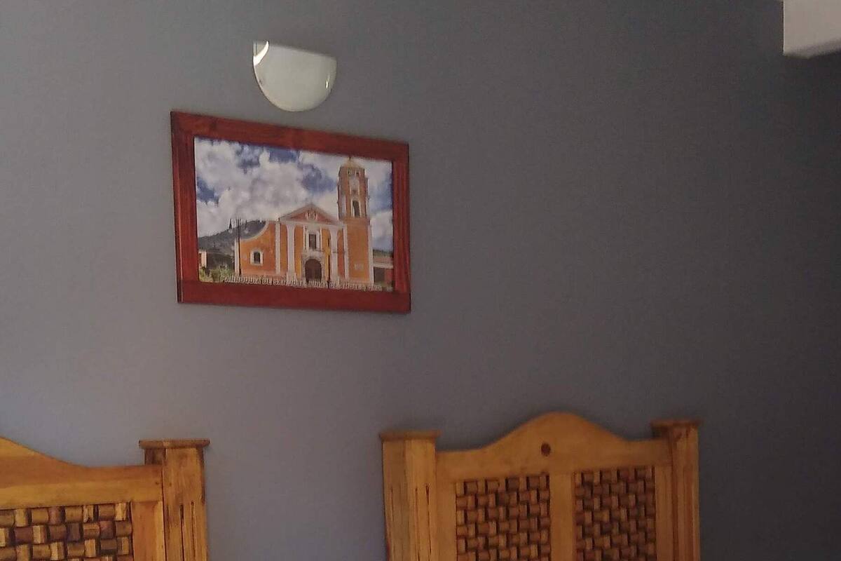 Une chambre d’hôtel avec deux lits en bois, une table de chevet, un tableau encadré au mur et un sol carrelé.