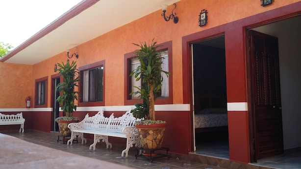 Un bâtiment à l’extérieur rouge et blanc, avec un patio couvert doté d’un banc blanc et deux plantes en pot.