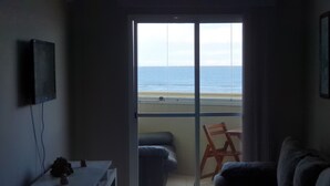 A room with a view of the sea through a large window, a chair, and a couch. - Beachfront apartment with a privileged ocean view. (SP)