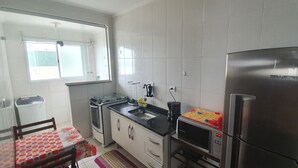 A compact kitchen with white tiles, a stainless steel refrigerator, a microwave, and a small sink. - Beachfront apartment with a privileged ocean view. (SP)