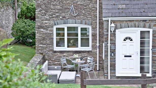 A stone building with a white door, a window with a white frame, and a small table with chairs outside. - Free Parking - Free Wi-Fi - 2km From The Beach (Strete)