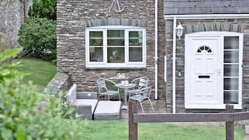 Un bâtiment en pierre avec une porte blanche, une fenêtre à cadre blanc et une petite table avec des chaises à l’extérieur.