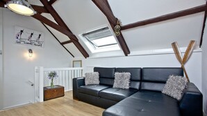 A modern loft-style room with a black leather sectional sofa, wooden beams, a skylight, and a 'Welcome Aboard' sign. - Free Parking - Free Wi-Fi - 2km From The Beach (Strete)