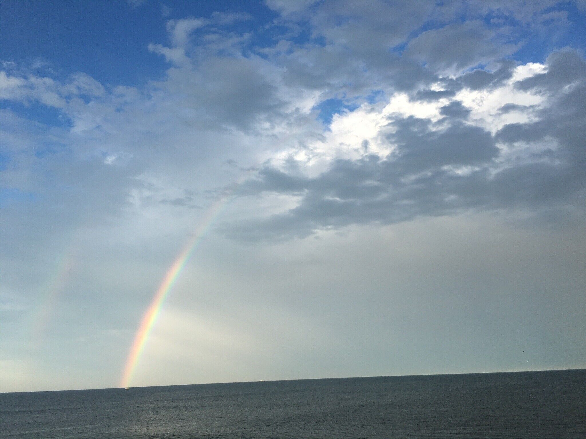 Un arc-en-ciel au-dessus de l’océan, sous un ciel nuageux.