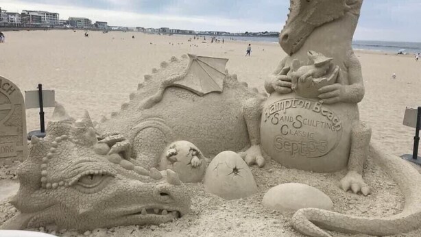 Une sculpture de sable représentant un dragon et un cheval, réalisée sur une plage, avec une pancarte indiquant : « Hampton Seaforth Classic Sand Sculpting ».