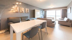 A modern living room with a dining area, a sofa, a coffee table, and artwork on the wall. - Calista 213 with balcony by Interhome (Bredene)
